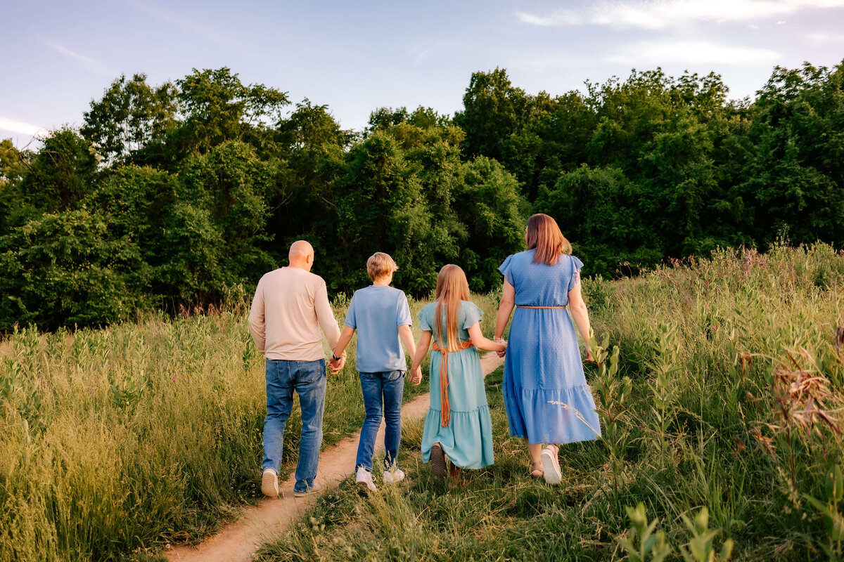 A gorgeous family of four walk hand in hand away from the camera at sunset.