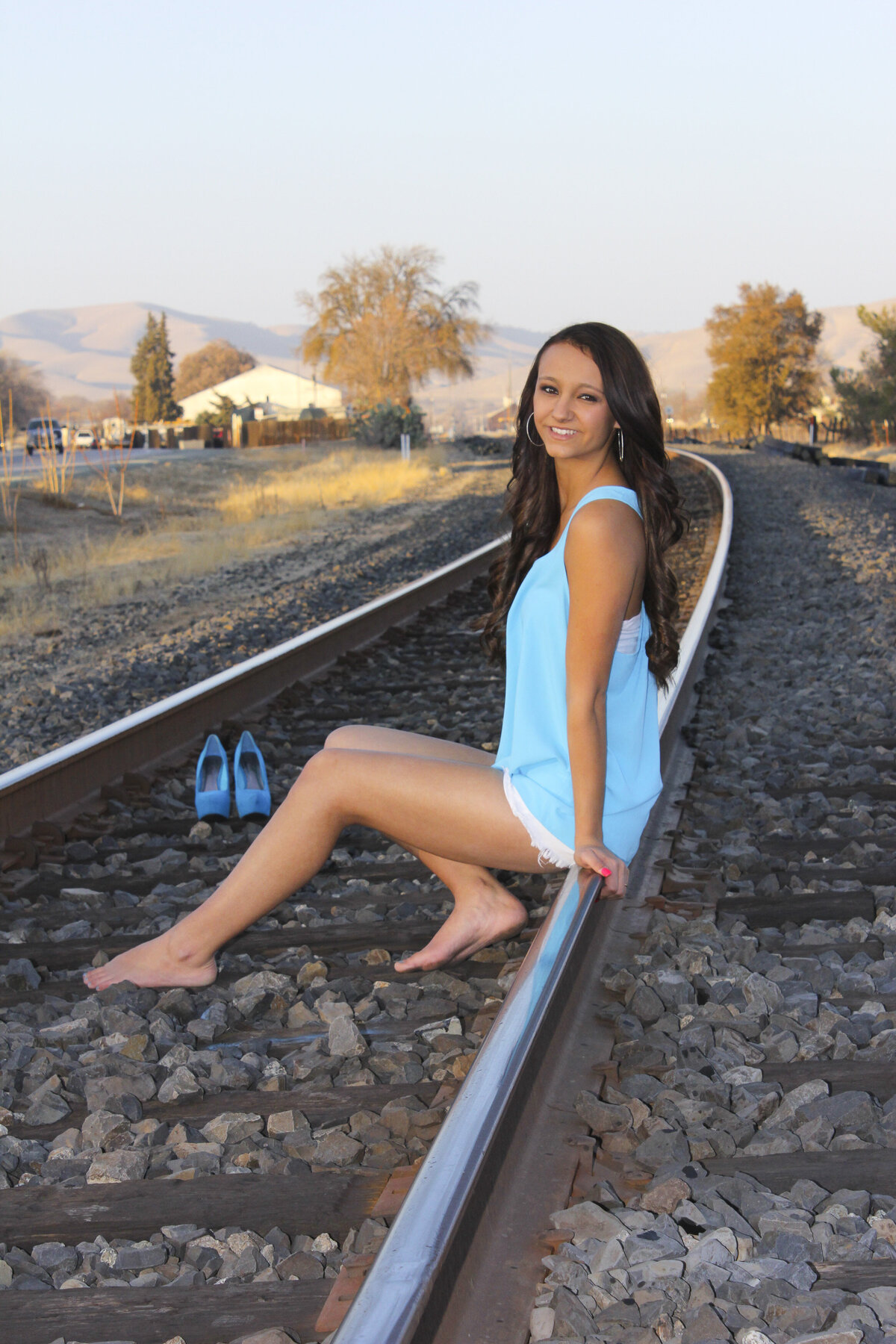 Lady sitting on Railroad tracks  with golden light of sunset beaming down with blue high heal shoes in background