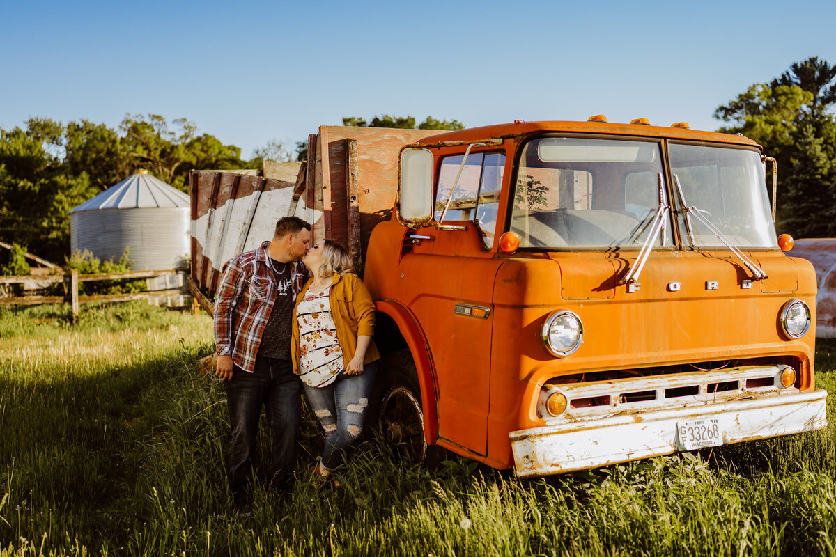 couple in front of old orange truck in field