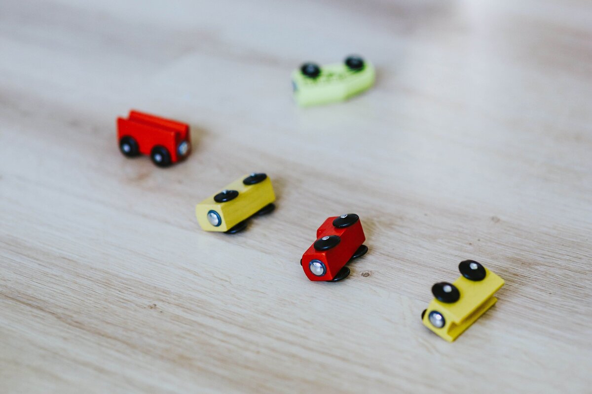 Colorful wooden toy cars scattered on a light wooden floor.