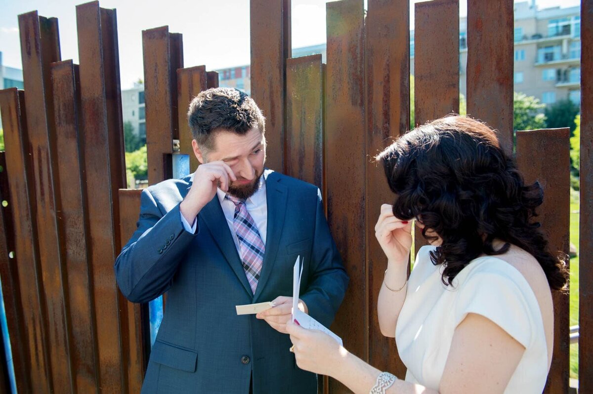 a bride and groom both wipe tears away as they read letters from each other