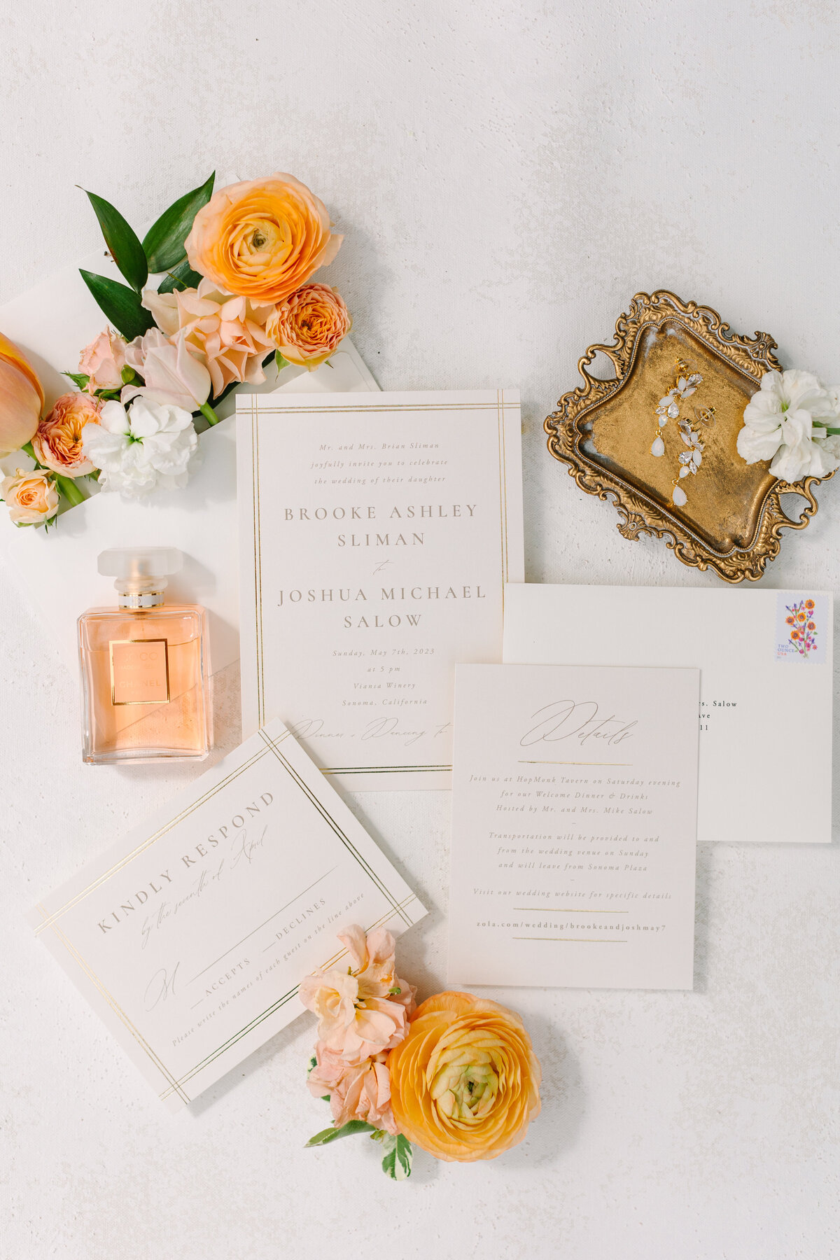 flat lay shot of wedding invitations, florals, perfume, and jewelry.