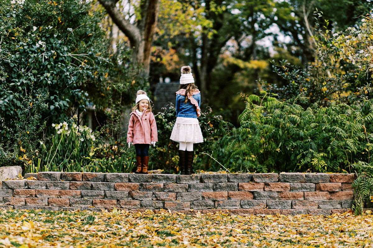 sisters stand on a brick wall during a fall photo shoot
