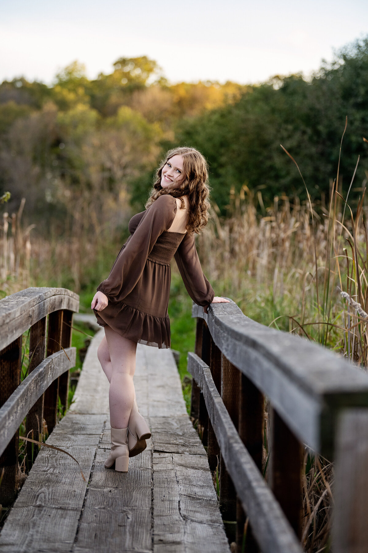 girl on old wooden bridge looking over her shoulder wearing a brown dress