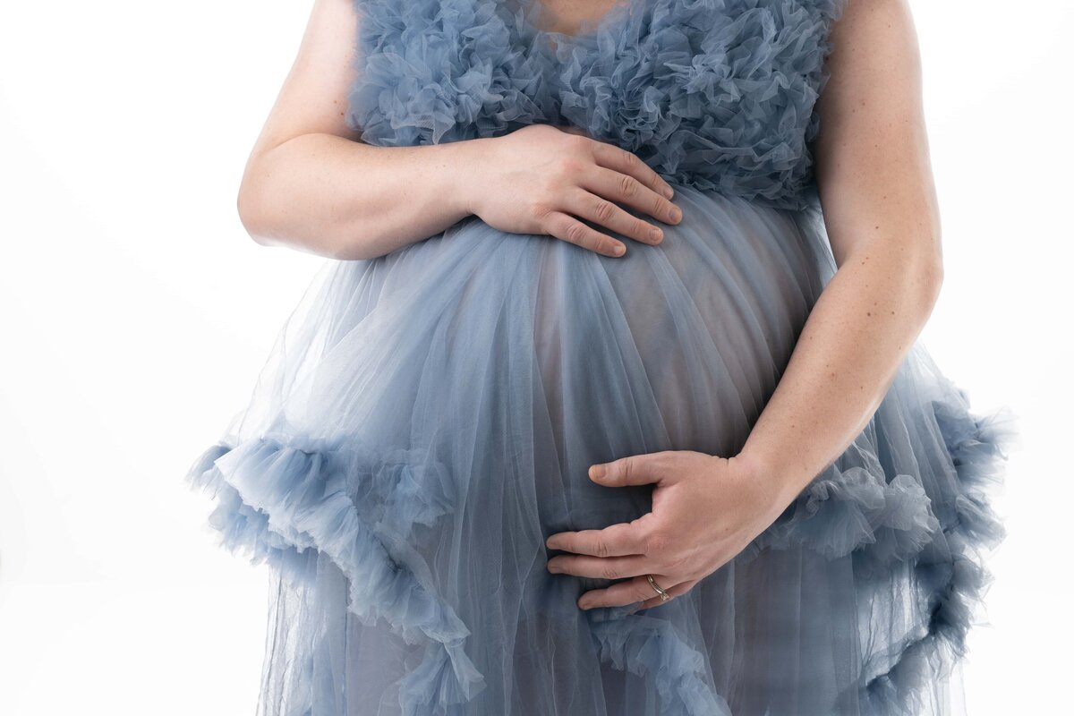 Blue maternity gown with hands on pregnant belly.