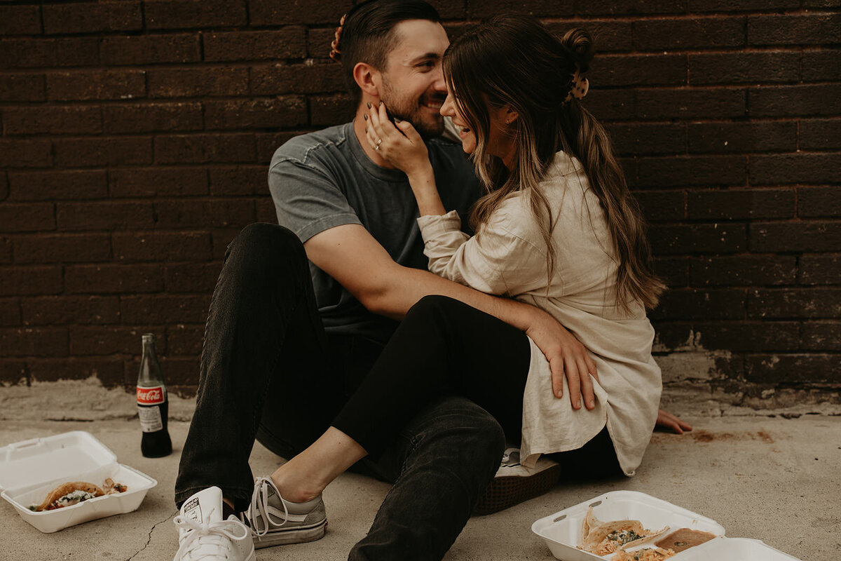 couple sitting against a wall holding each other and laughing