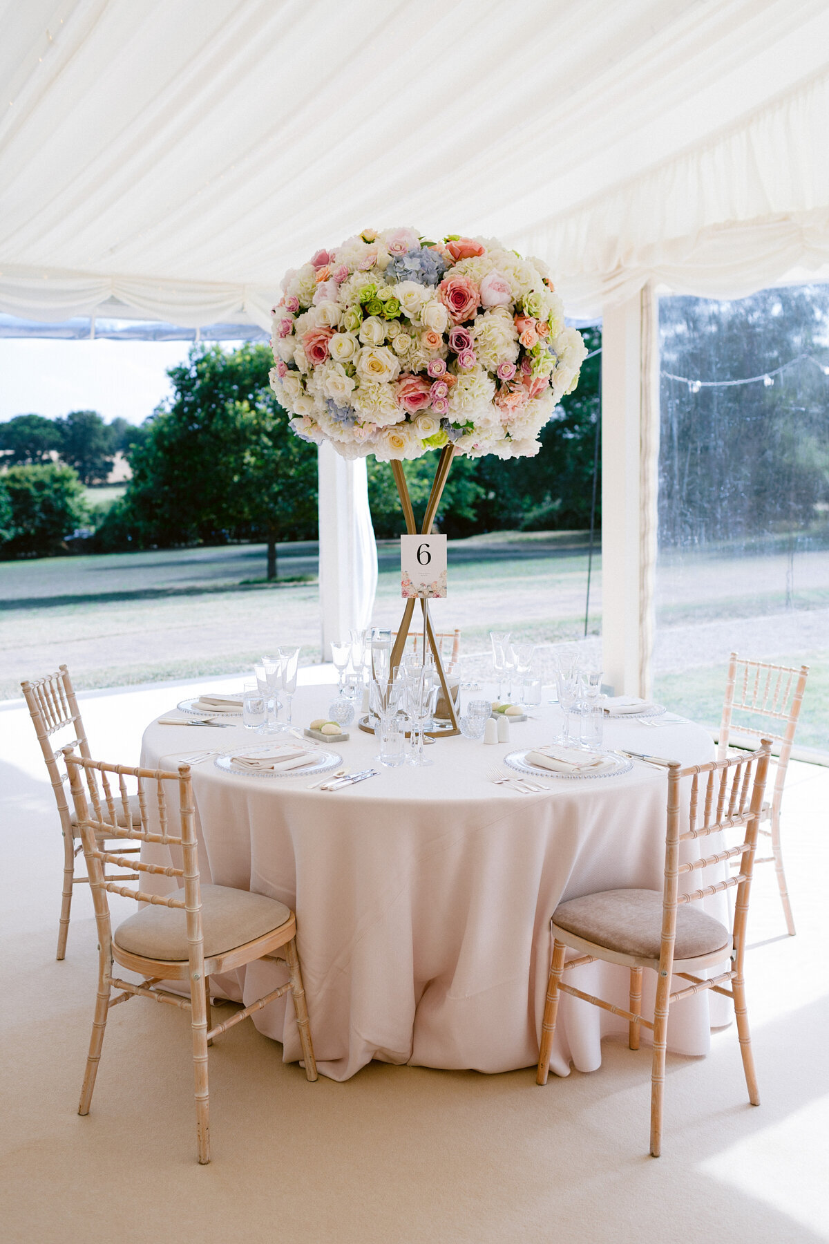 wedding table inside the marquee with tall artificial mixed flowers table arrangement and paper table number