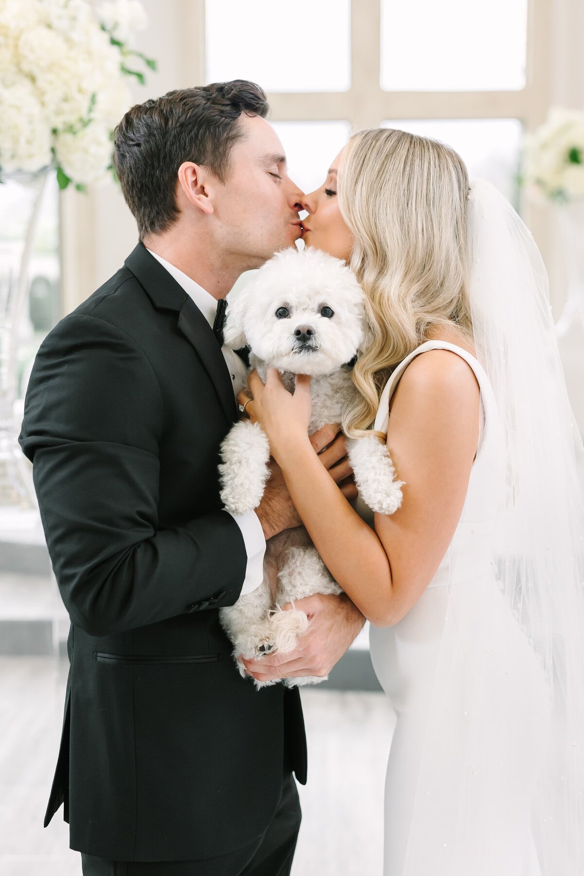 bride and groom hold dog and kiss