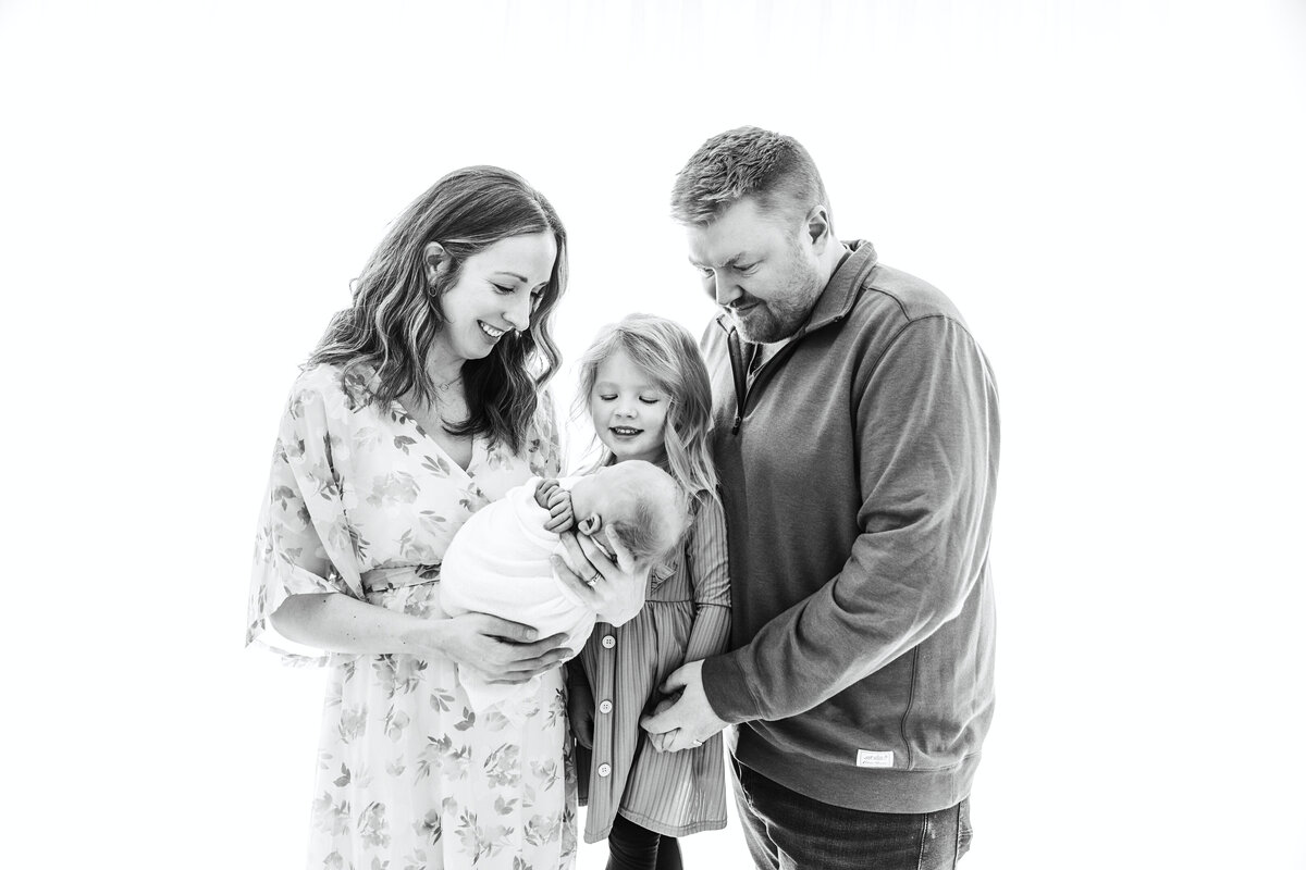 Mom, Dad and little girl looking down at swaddled baby, taken by Fig and Olive Photography a Twin Cities Newborn Photographer
