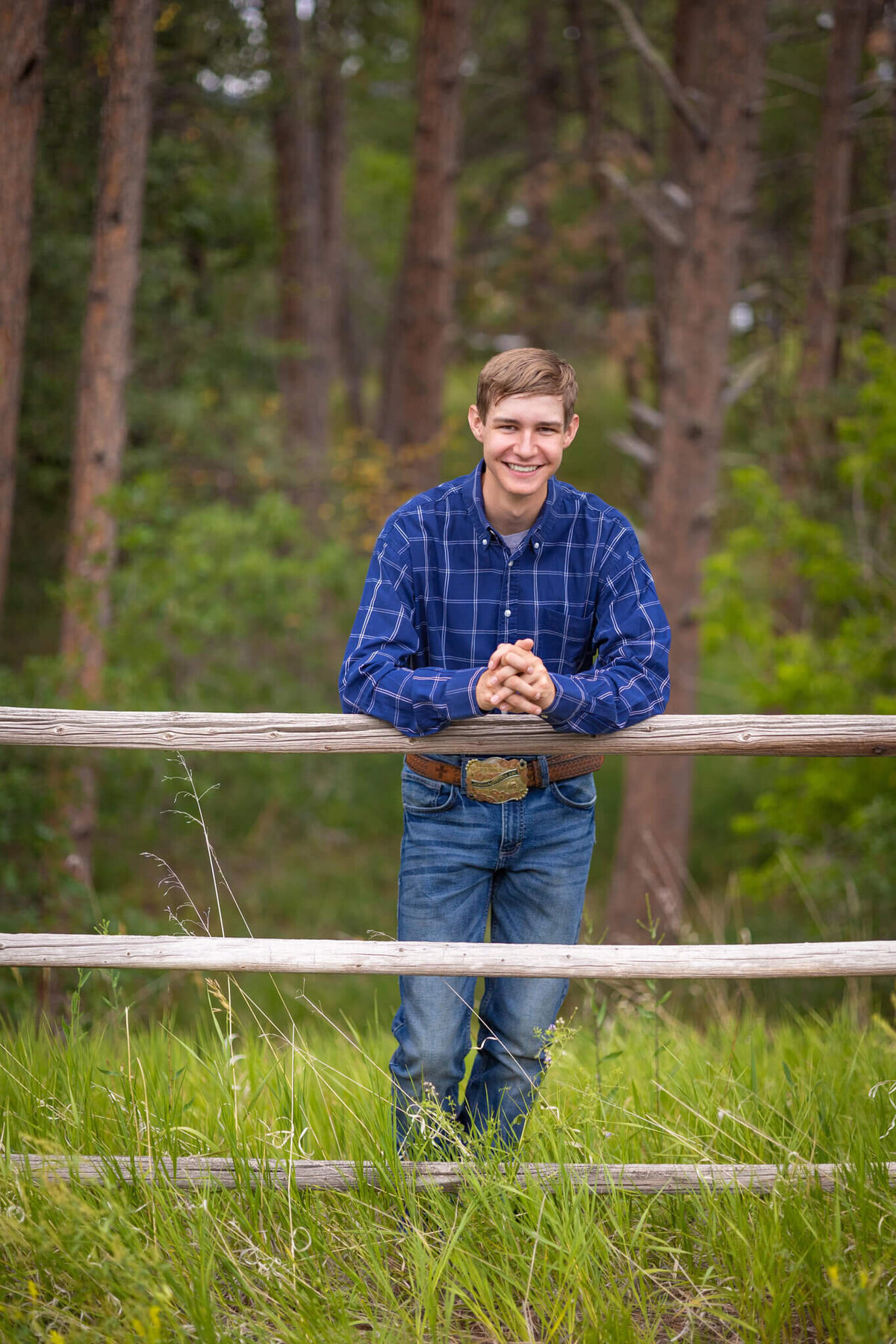 high school senior boy lin blue long sleeve shirt and jeans leaning against a wooden fence