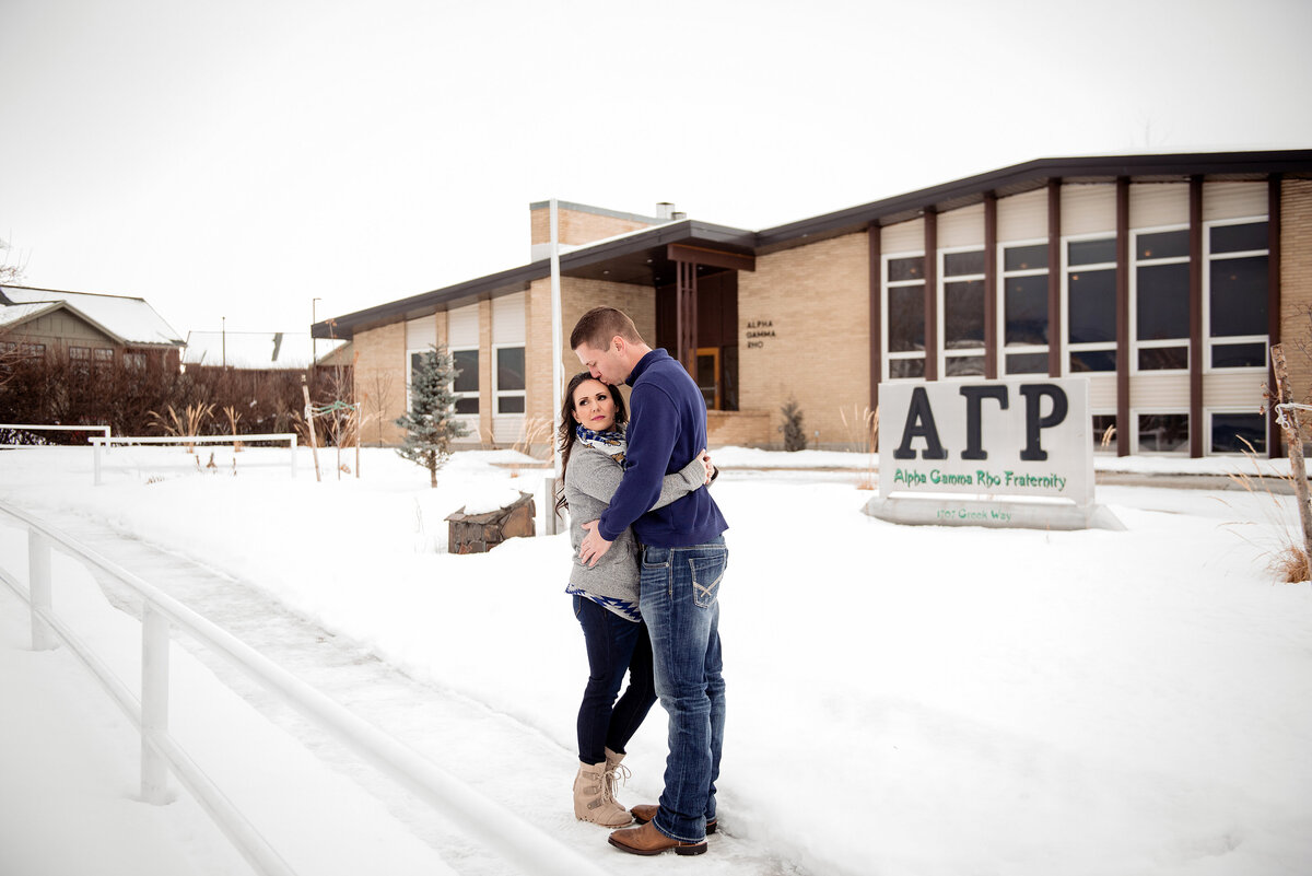 Engaged couple standing outside of the Alpha Gamma Rho chapter house at Montana State University with snow covered grounds