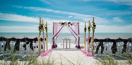 A square arch decorated with pink voile stands infront of the sea at the end of the aisle