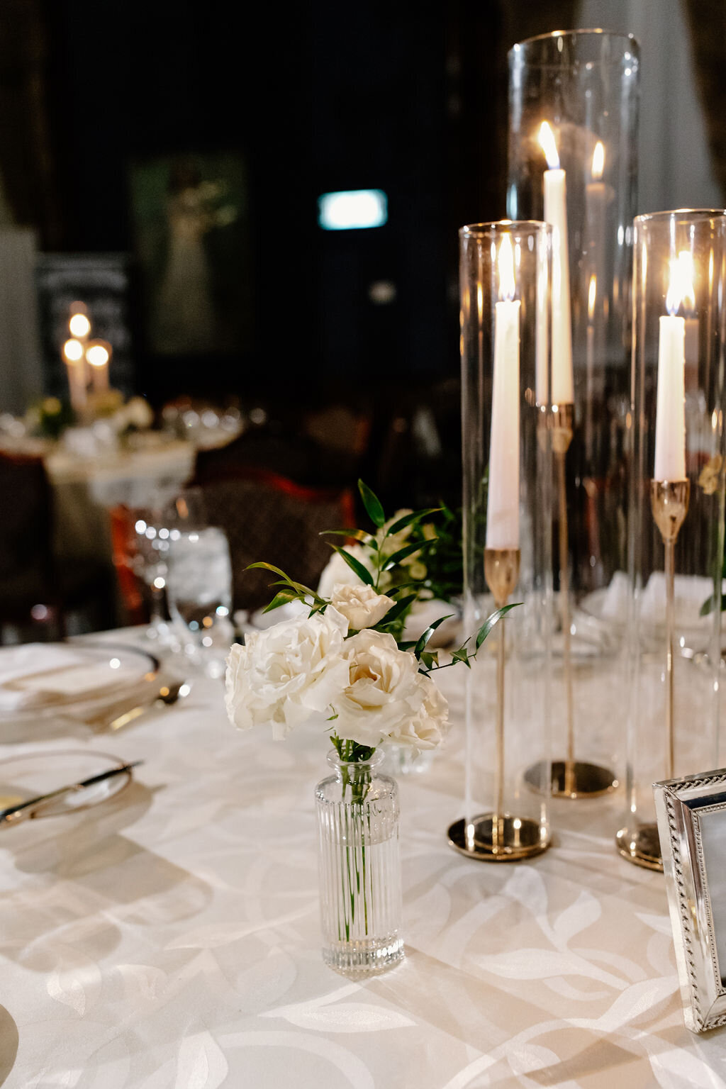Glass and gold candlesticks accompany a vase of elegant white roses for a class wedding centerpiece look.