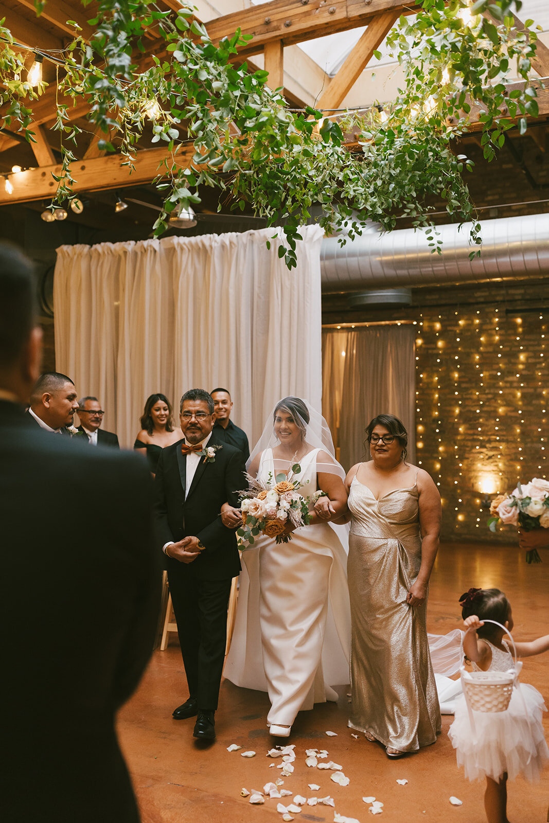 Bride in satin dress and veil is walked down aisle with mother and father at luxury Loft on Lake Chicago wedding.