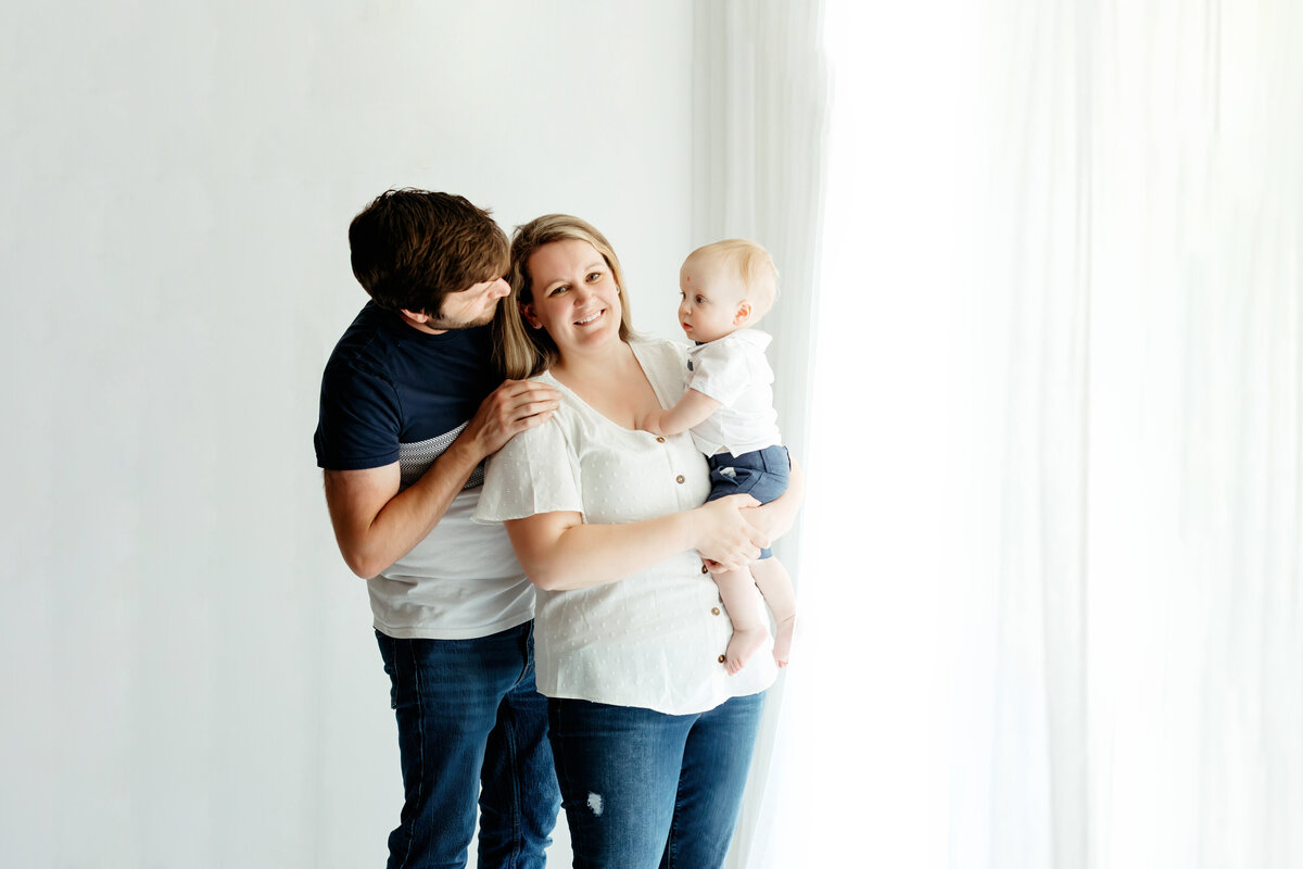 family of three standing near white curtains for indoor family photos