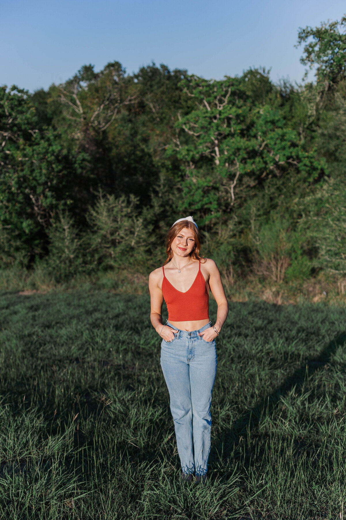 Santa Fe High School senior girl stands in a field wearing a red tank top and jeans