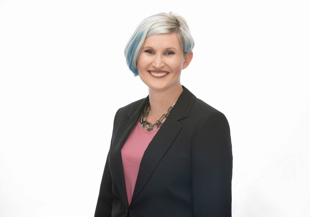 An executive businesswoman with short with blue hair and a black blazer poses for a professional headshot on a white background for Janel Lee Photography studios Cincinnati Ohio