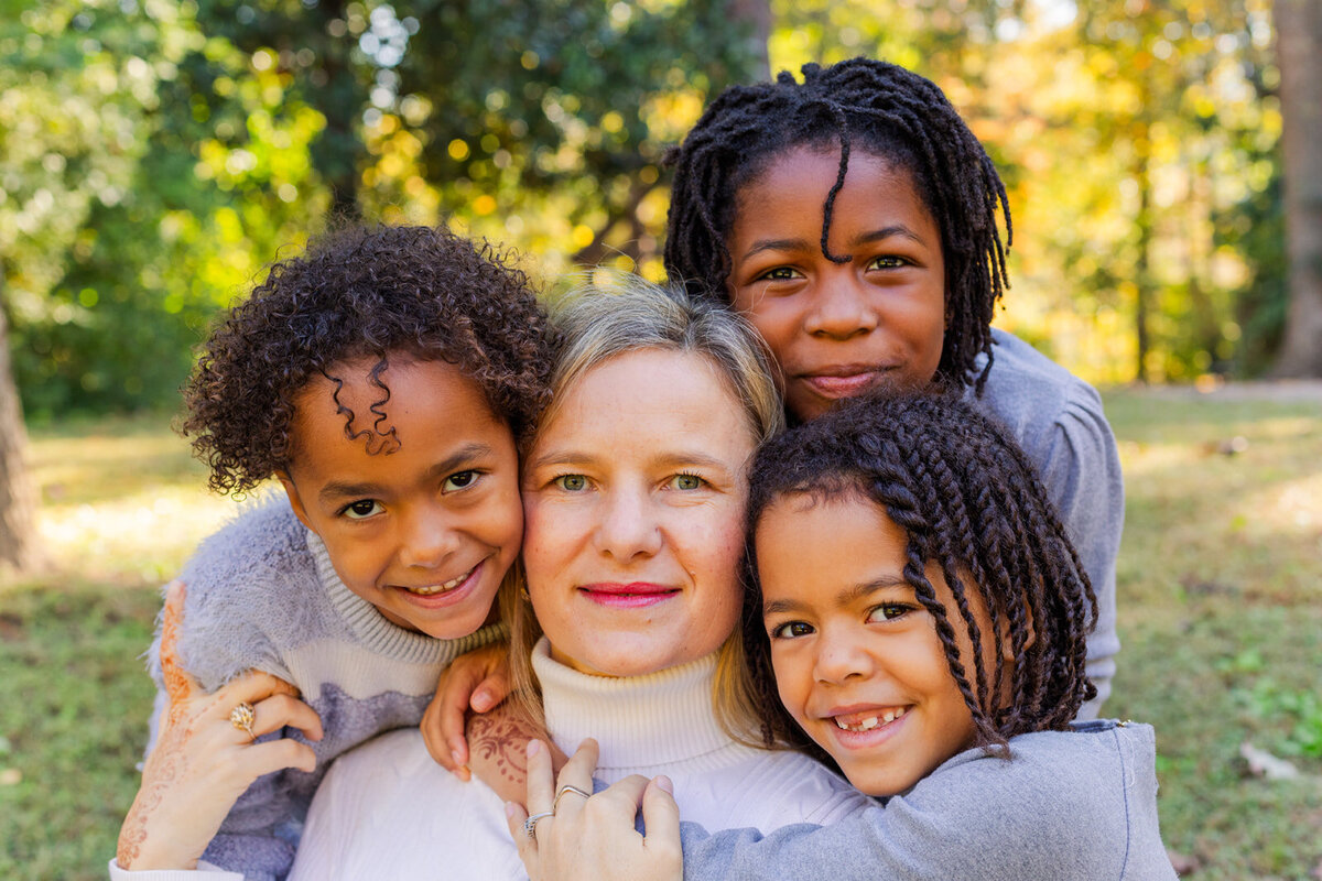 Mum surrounded by daughters faces hugging each other, mixed family sitting in Atlanta park by Laure Photography