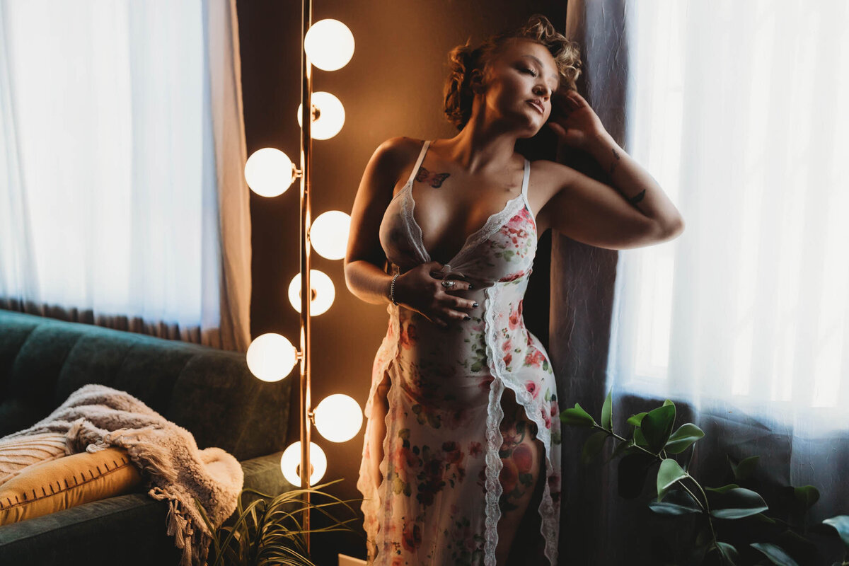 woman leaning against a window in long slip dress with moody lighting