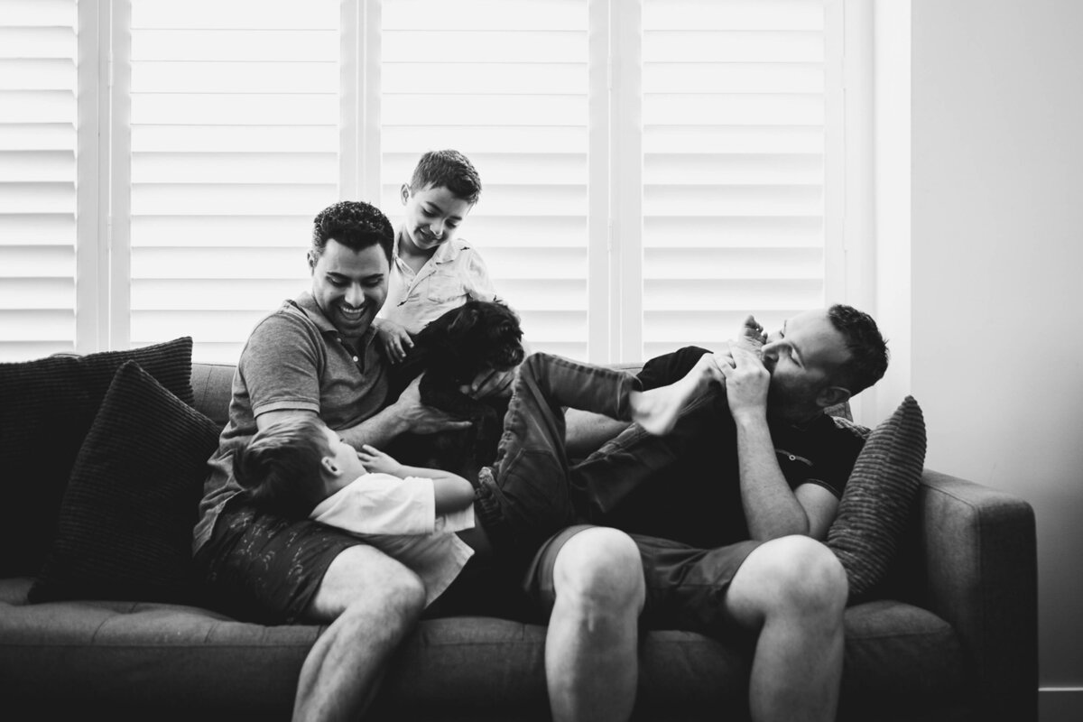 Two dads and their twin sons roughhouse on the couch during their at home family photography session with Marjorie Cohen.