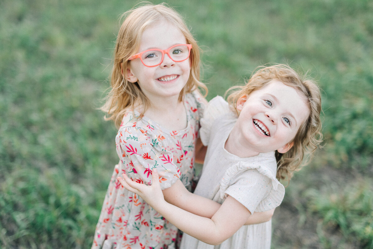 colorado wedding photographers captures two little children hugging each other in a green grass field and smiling up to the camera