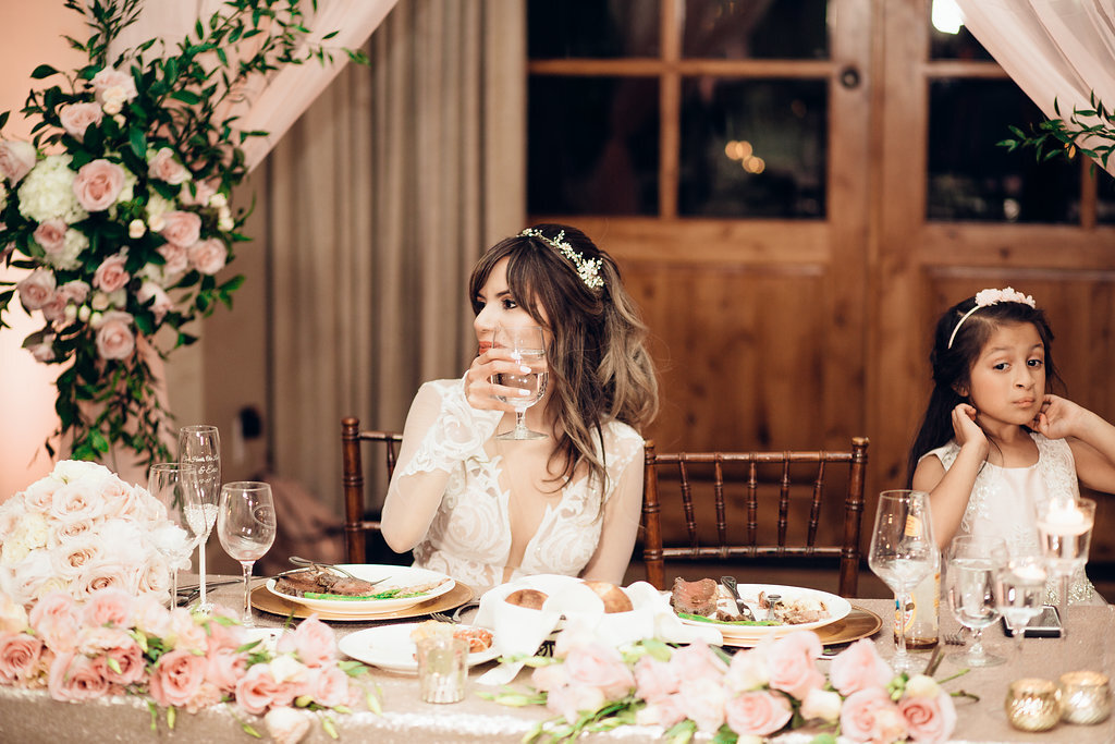 Wedding Photograph Of Bride Drinking From Her Wine Glass  While Seated Beside a Kid Los Angeles