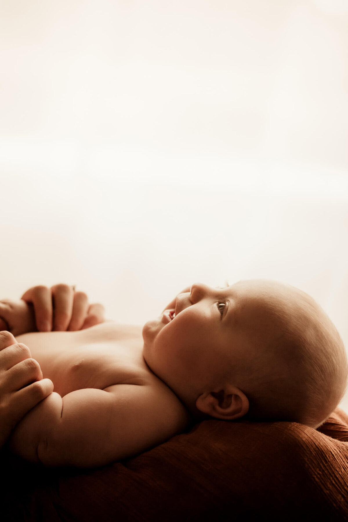 Baby boy looking up while laying on his mother's lap with a  window behind him for a studio photo in Tulsa, Okahoma.