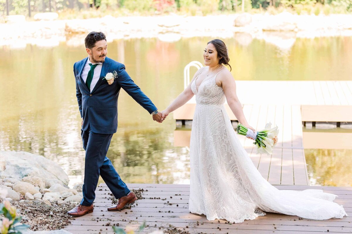 Groom, leading his bride across a dock, with water in the background