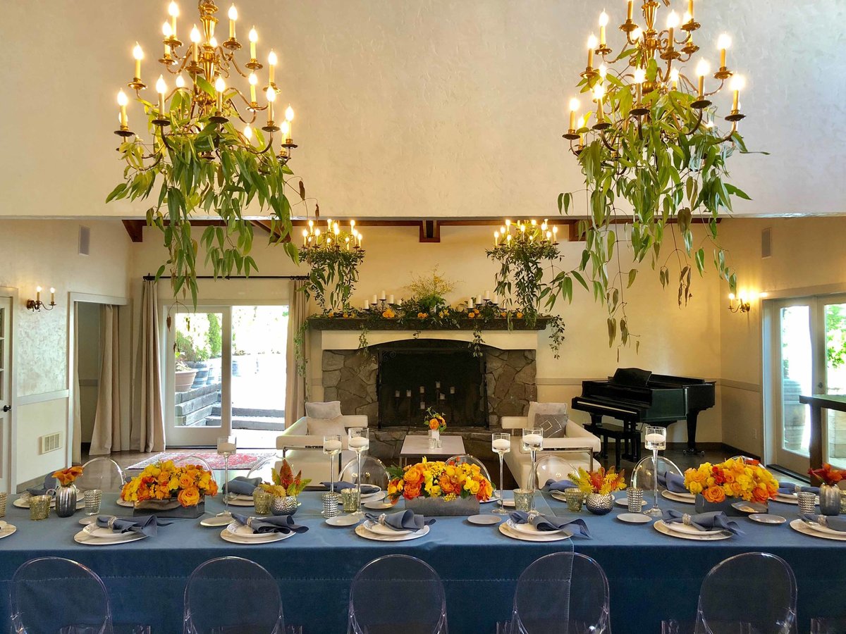 trailing greenery from chandeliers above dinner table  lined with orange flower centerpieces at Chateau lill