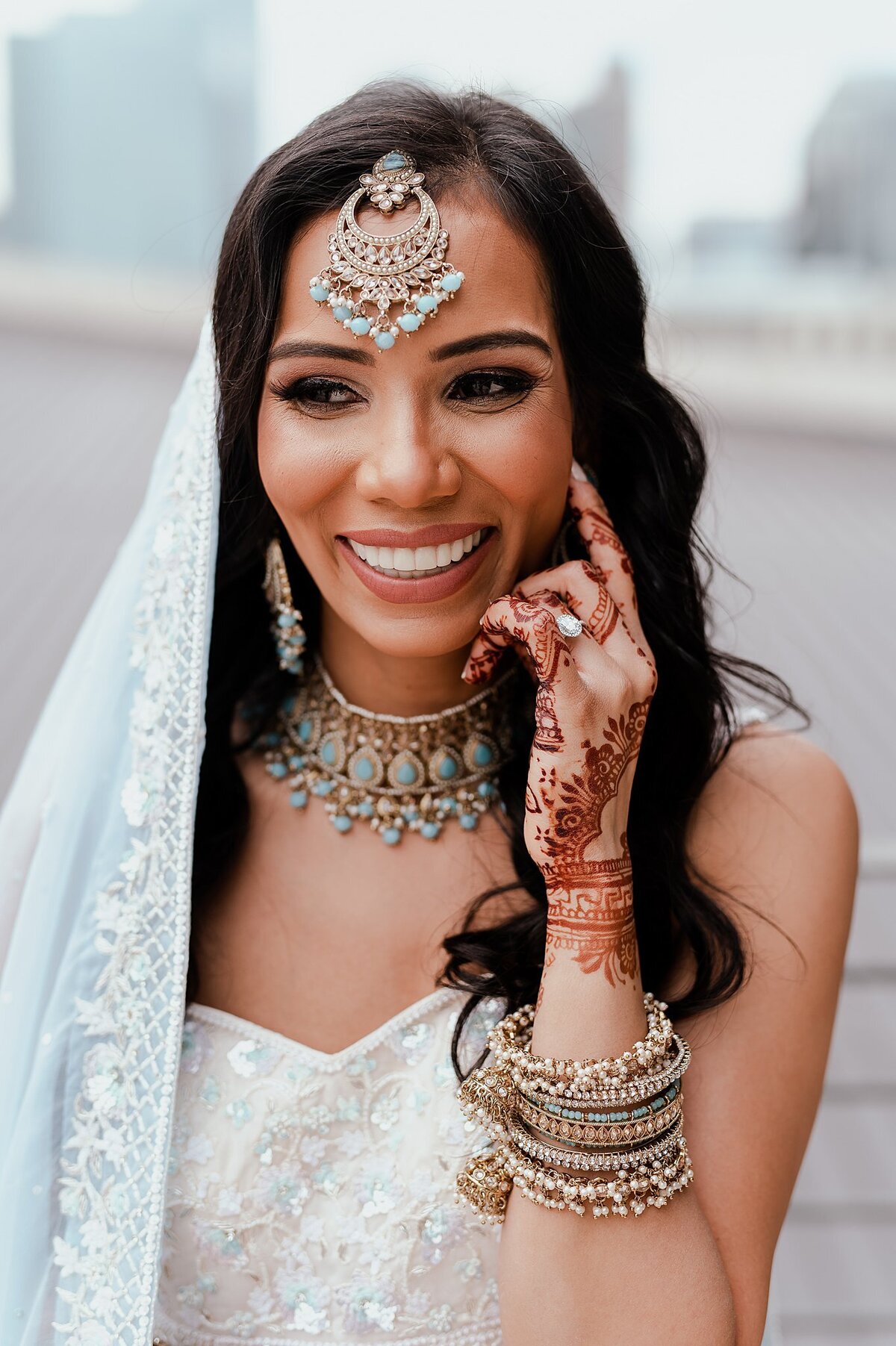 Hindu bride wearing a beaded white and light blue wedding saree shows off her blue and gold wedding jewelry and the mendhi on her hands in Nashville, TN at the Country Music Hall of Fame