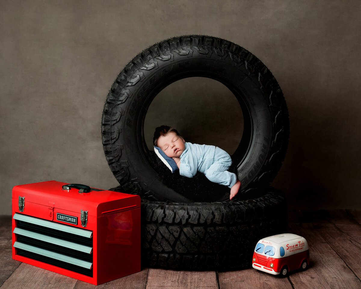 Baby lies in tire for cute mechanic theme newborn photo in Syracuse New York