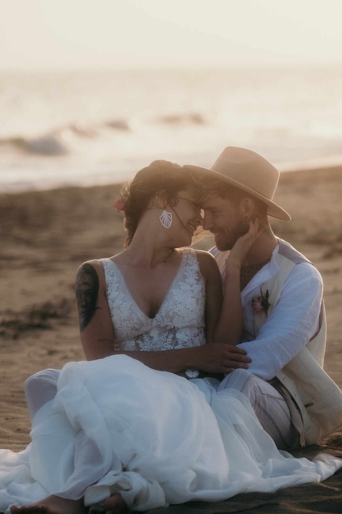 Glücklich lächelnd blickt sich das verliebte Hochzeitspaar am Strand sitzend tief in die Augen.