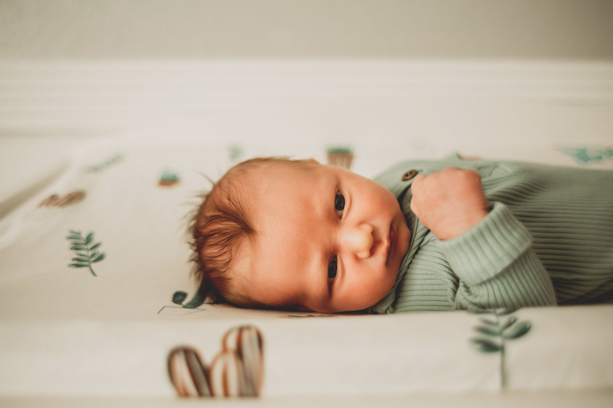 newborn baby boy laying on changing table wearing a lgith green sleper
