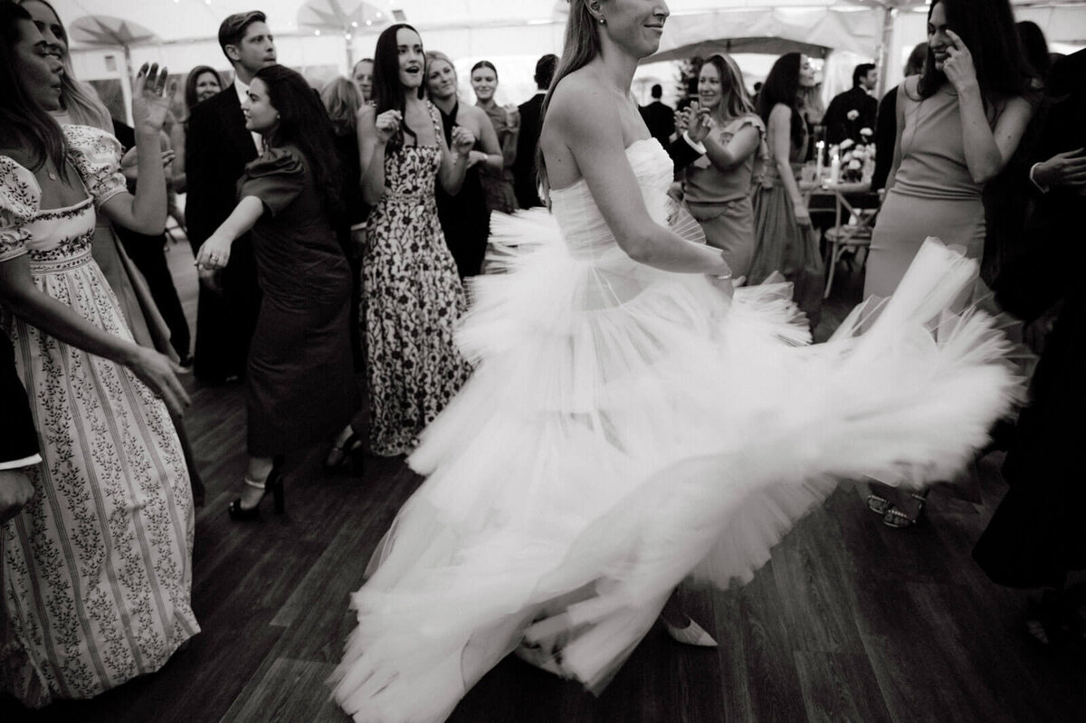 The bride, with her beautiful gown flowing, is dancing with the guests at The Ausable Club, NY. Image by Jenny Fu Studio