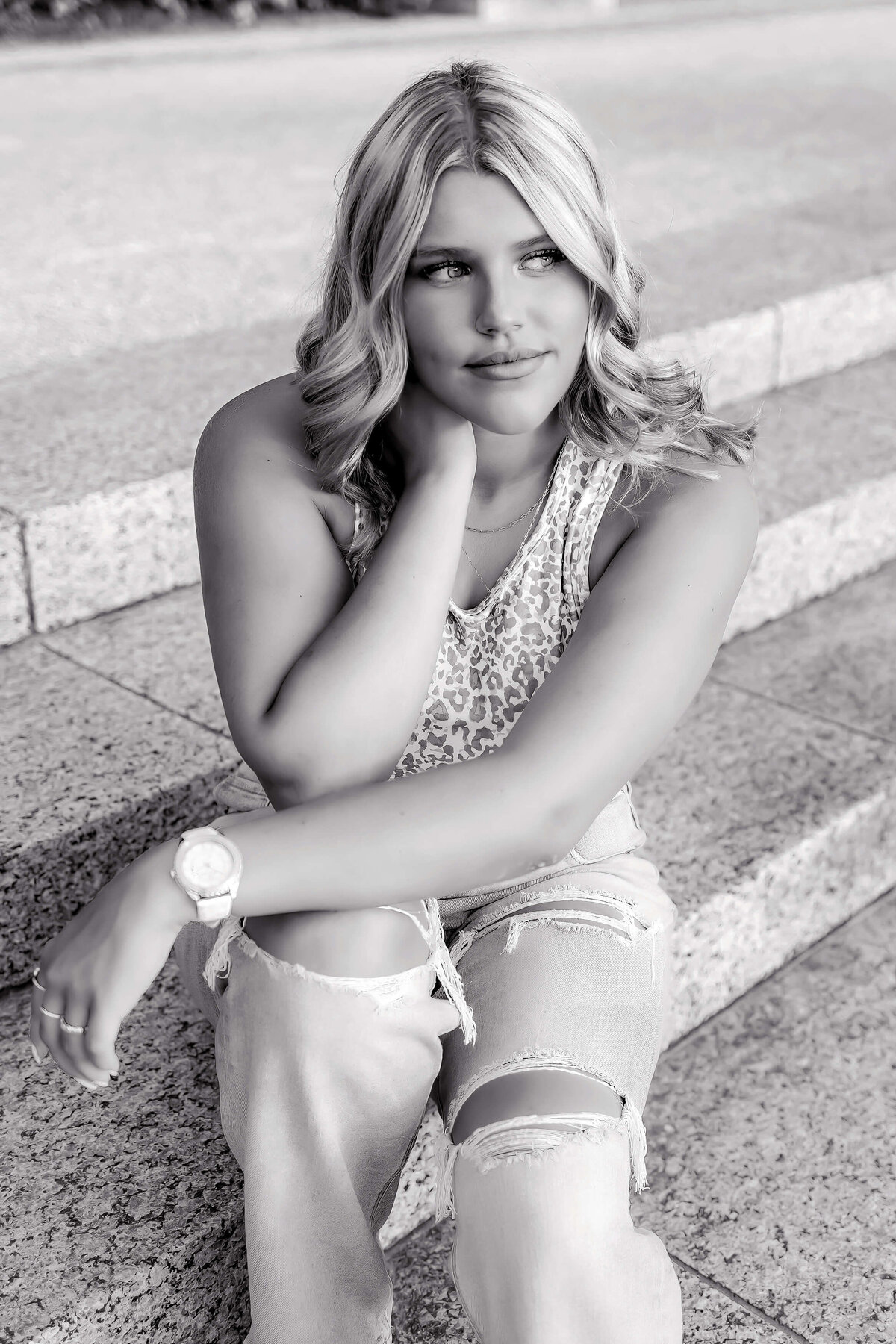 a beautiful blonde haired high school senior girl sitting on concrete steps outdoors in black and white
