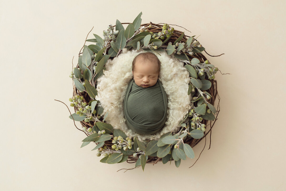 A newborn baby sleeps in a sage swaddle surrounded by a green wreath