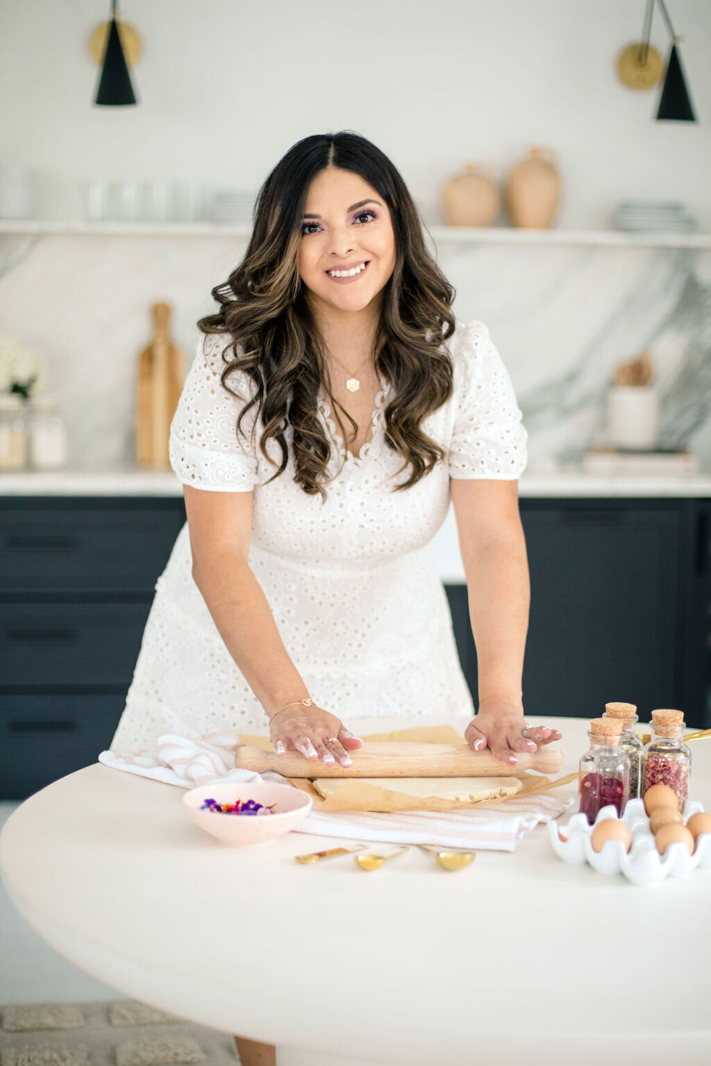 woman rolling out dough with petals, eggs, and tools spread out on table