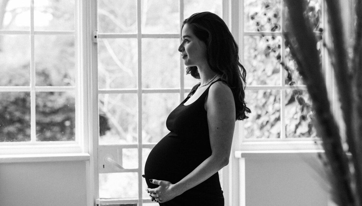 Black and white image of woman in a black dress, pregnant and holding her belly