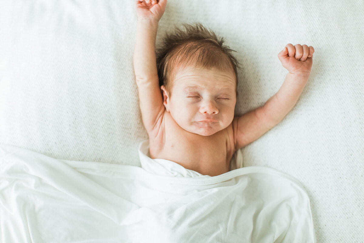 Newborn baby stretches his arms above his head
