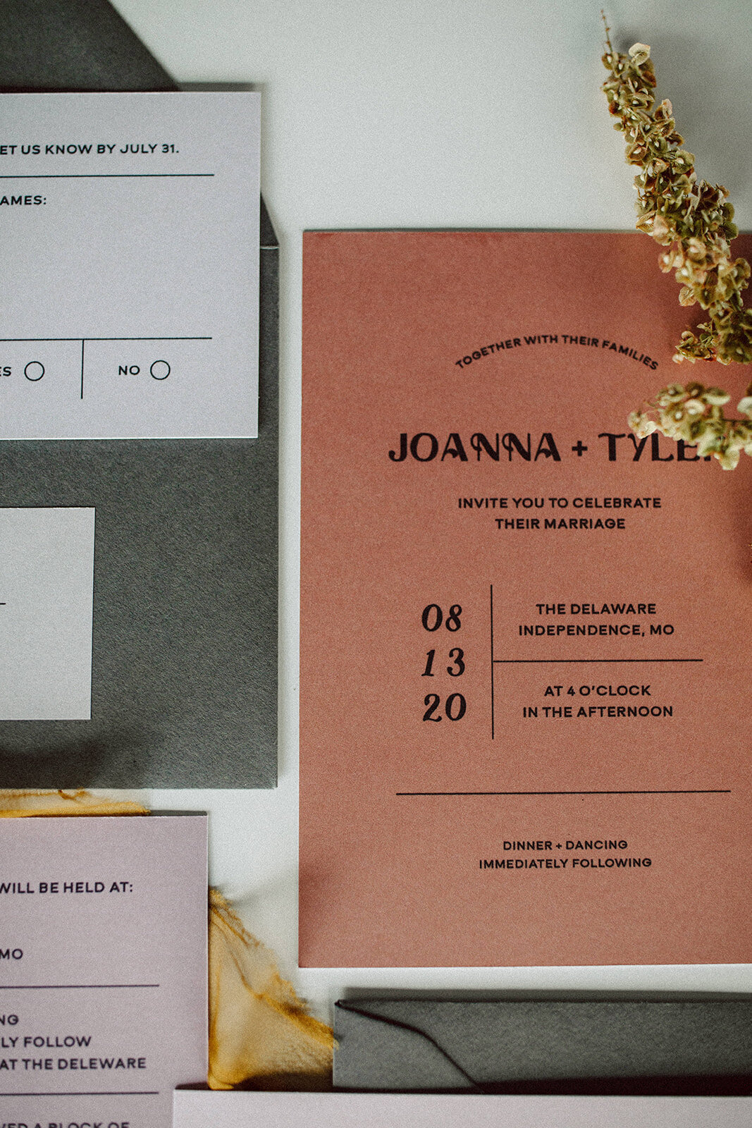 Peach wedding invitation with black font next to light gray and mauve-colored wedding stationery atop white table.