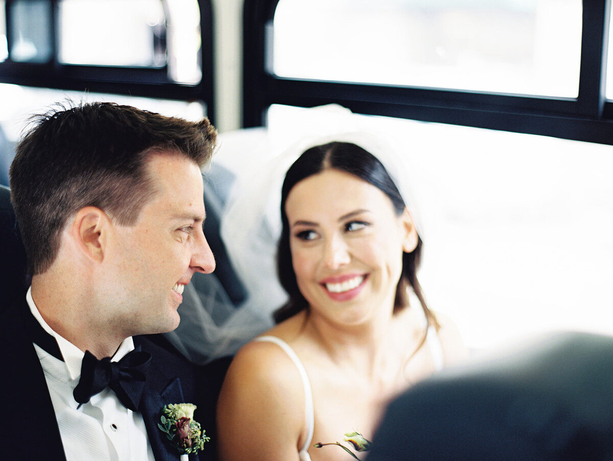bride looking at groom as they sit on the bus taking them to their ceremony spot