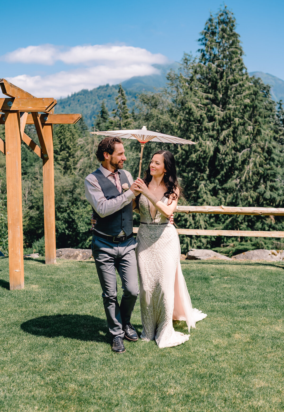 Bride and groom holding a Japanese umbrella, walking and looking at each other. Greenery and  mountain view in the back round.