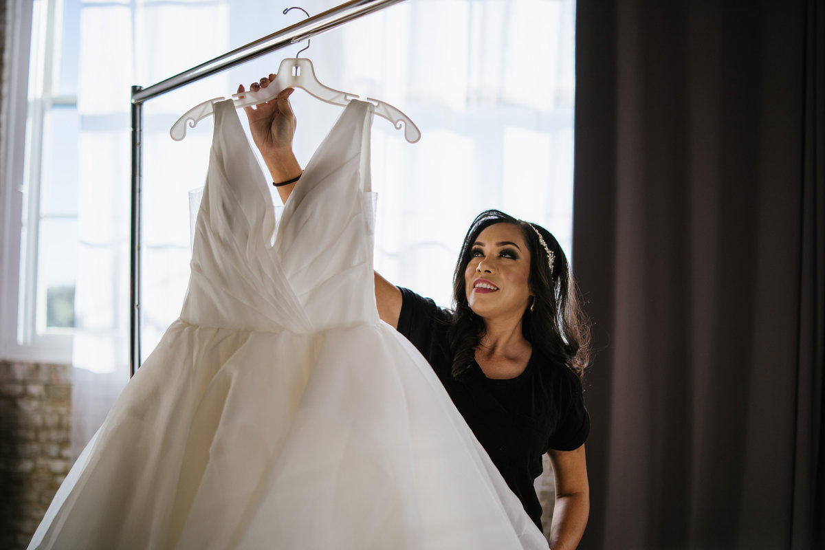 Bride getting ready to put on bridal gown before wedding ceremony taking dress off rack.