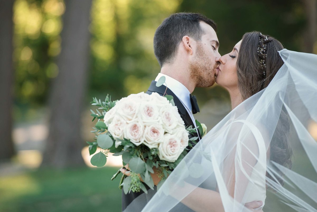 Bride and groom kissing outdoors with veil on and bouquet in hand at Stonebridge Country Club