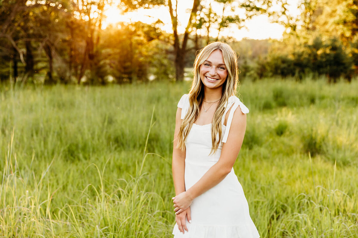 young woman in a white dress holding her hand as the sun sets behind her