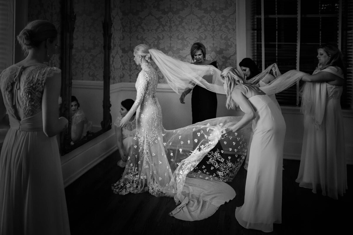 A monochrome image of bridesmaids in elegant dresses fluttering the bride's veil