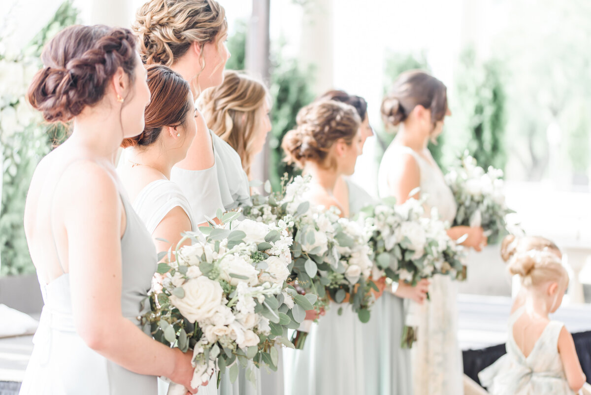 bridesmaids in pale green dresses and holding ivory bouquets are turned towards the bride and groom during the ceremony