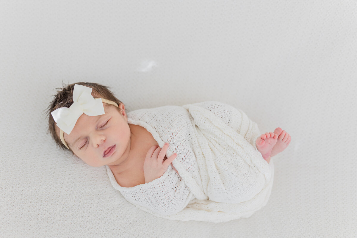 solo portrait of a newborn baby girl whose swaddled in a cream colored print and is sleeping