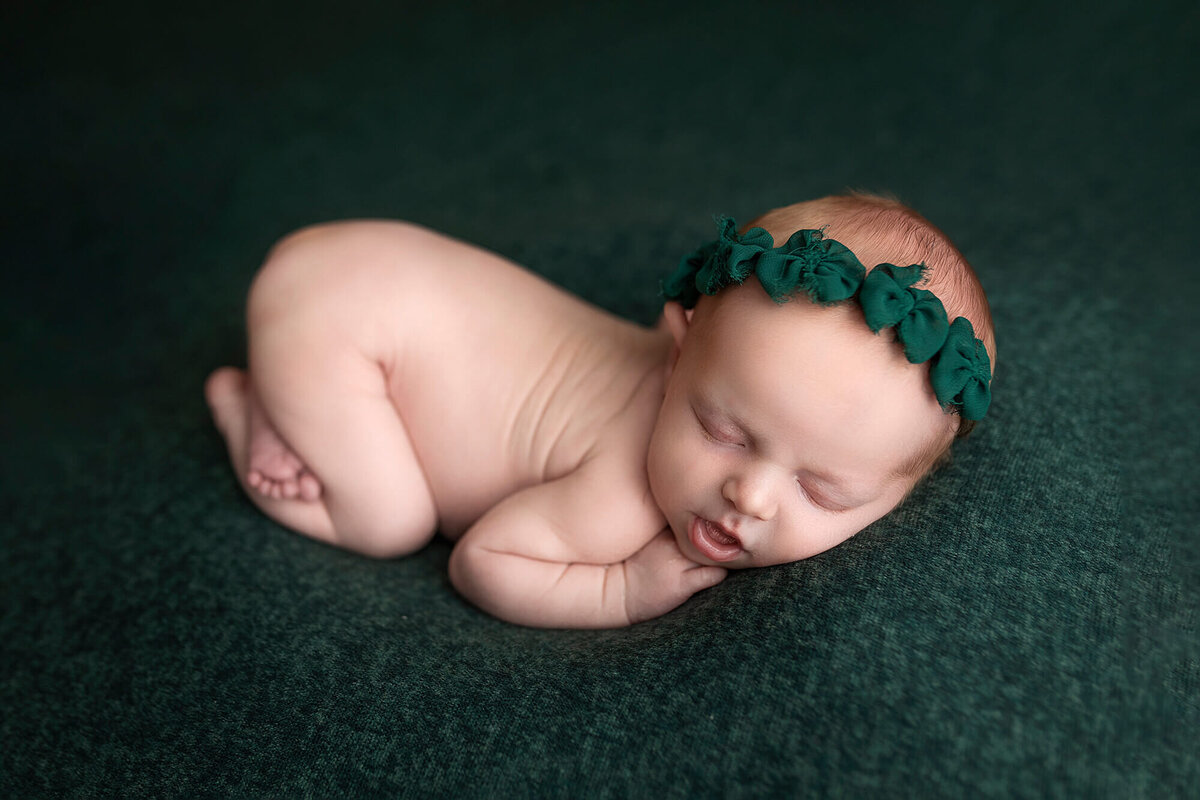 Newborn girl posed on dark green wearing a matching bow headband.