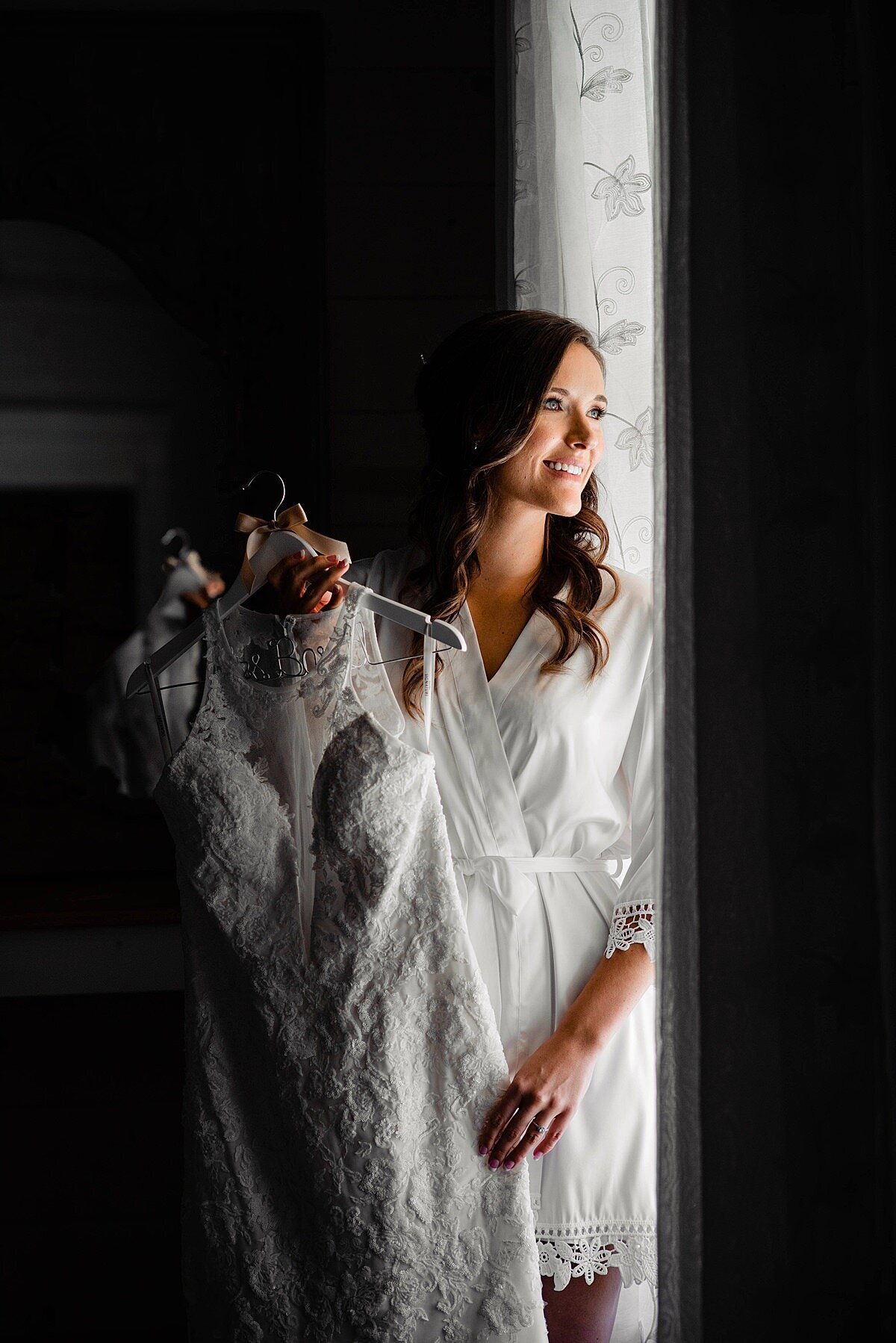 Bride holding dress while looking out the window